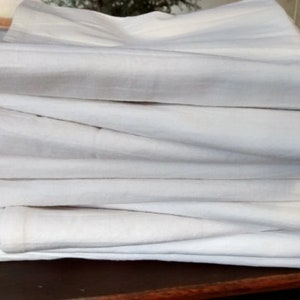 May include: A stack of white cotton dish towels folded neatly on a wooden surface.
