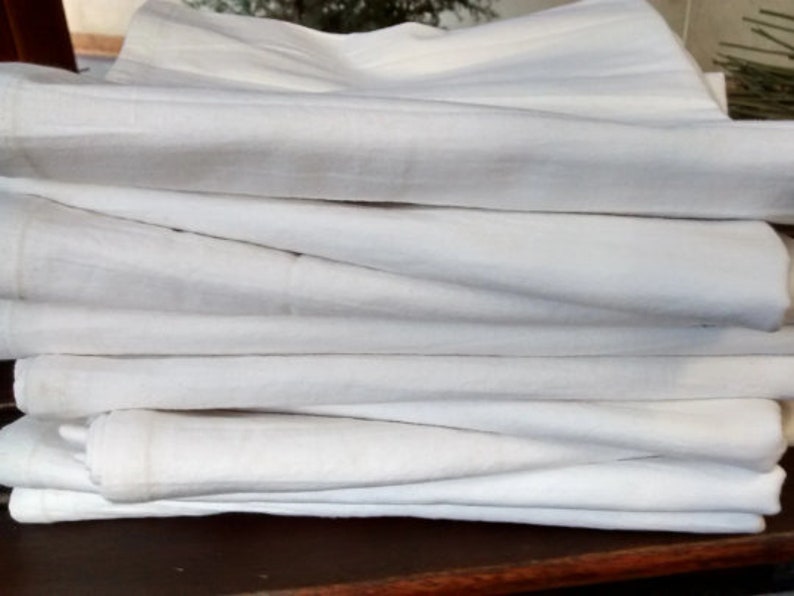 May include: A stack of white cotton dish towels folded neatly on a wooden surface.