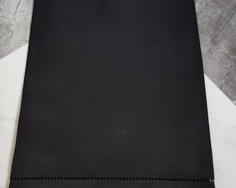 May include: A solid black rectangular textile with a row of small, evenly spaced holes near the bottom edge. The fabric appears to be smooth and opaque, with a matte finish. The background is a mix of white and gray geometric shapes.