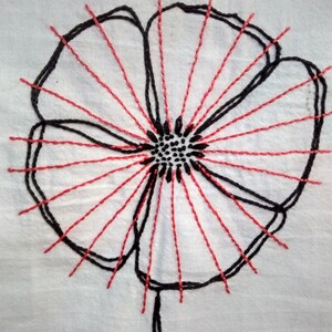 Könnte beinhalten: Eine gestickte Blume in Schwarzweiß mit roten Nähten, die vom Zentrum ausstrahlen.