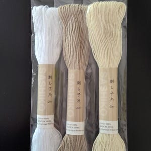 Puede incluir: Tres bobinas de hilo Sashiko en un paquete de pl&aacute;stico transparente. Los colores del hilo son blanco, marr&oacute;n y crema. Cada bobina tiene una etiqueta de papel con texto japon&eacute;s y el nombre de la marca. El hilo es 100% algod&oacute;n y est&aacute; hecho en Jap&oacute;n.