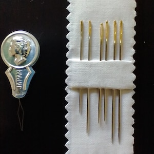 Op de afbeelding: Een set van acht goudkleurige naalden in een wit stoffen etui met gegolfde randen. Het etui heeft de tekst "JAPAN" erop gedrukt.
