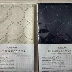 K&ouml;nnte beinhalten: Zwei verpackte Baumwoll-/Leinen-Sashiko-Stoffe. Einer ist cremefarben mit grau gen&auml;hten Kreisen, der andere marineblau mit wei&szlig; gen&auml;hten Kreisen. Jede Packung hat Text in Japanisch und Englisch, einschlie&szlig;lich der Marke "cosmo".