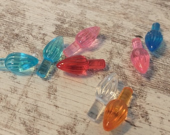 May include: Assortment of colorful plastic Christmas light bulb covers. The covers are in various colors, including red, orange, yellow, green, blue, and pink. The covers are scattered on a wooden surface.