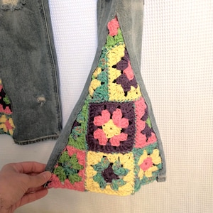 May include: Light blue denim jeans with distressed details and colorful crochet patchwork on the flared leg openings. The crochet features squares in pink, yellow, green, and purple.