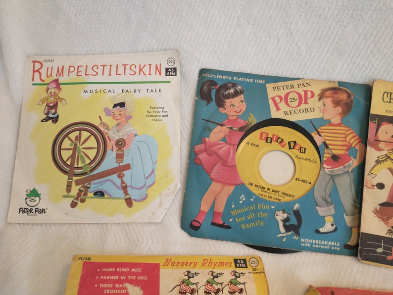 May include: A collection of vintage children's records featuring fairy tales and nursery rhymes. The records are in colourful cardboard sleeves with illustrations of the stories. The sleeves are labelled with the titles "Rumpelstiltskin", "Peter Pan Pop Record", "Nursery Rhymes", and "Children's Songs".