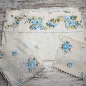 May include: A set of three white cotton pillowcases with a blue floral pattern. The pillowcases feature a border of blue roses and leaves.