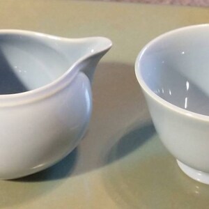 May include: A set of two light blue ceramic teacups. The creamer has a rounded shape with a handle. The teacup has a rounded shape with a handle.