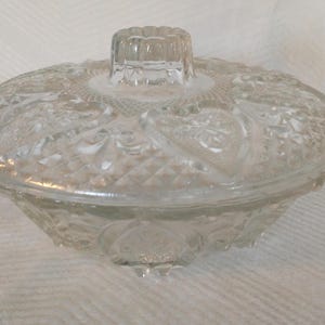 May include: A clear glass candy dish with a lid. The dish has a decorative pattern of flowers and leaves. The lid has a knob on top.