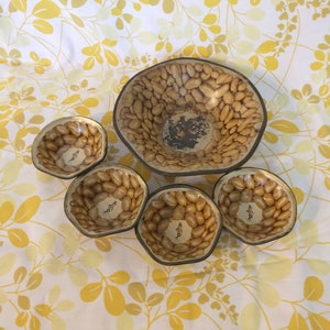 May include: A set of five peanut-shaped bowls, with a larger bowl in the center. The bowls are made of ceramic and have a brown and white peanut design. The bowls are perfect for serving snacks or dips.