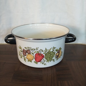 May include: White enamel pot with black handles and a colorful vegetable design. The design features a red pepper, yellow lemon, green artichoke, and brown mushrooms.