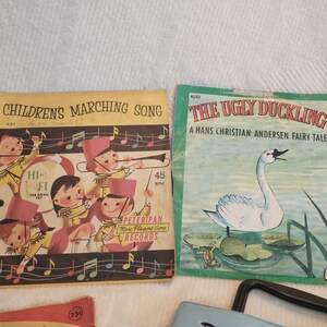 May include: Two vintage children's record albums. The first album is titled "Children's Marching Song" and features a colourful illustration of children in a marching band. The second album is titled "The Ugly Duckling" and features a colourful illustration of a swan swimming in a pond.