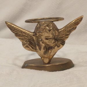 May include: A gold metal angel figurine with wings outstretched, holding a halo above its head. The angel is standing on a round base.