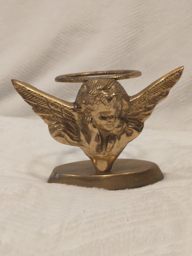 May include: A gold metal angel figurine with wings outstretched, holding a halo above its head. The angel is standing on a round base.