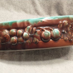 May include: A brown and green ceramic serving dish with a raised design of grapes and leaves around the rim.