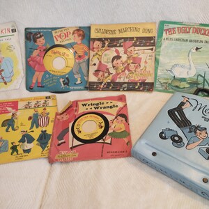 May include: A collection of vintage children's record players and records. The records feature colourful covers with illustrations of children and animals. The record players are blue and black with a design of a girl listening to music.