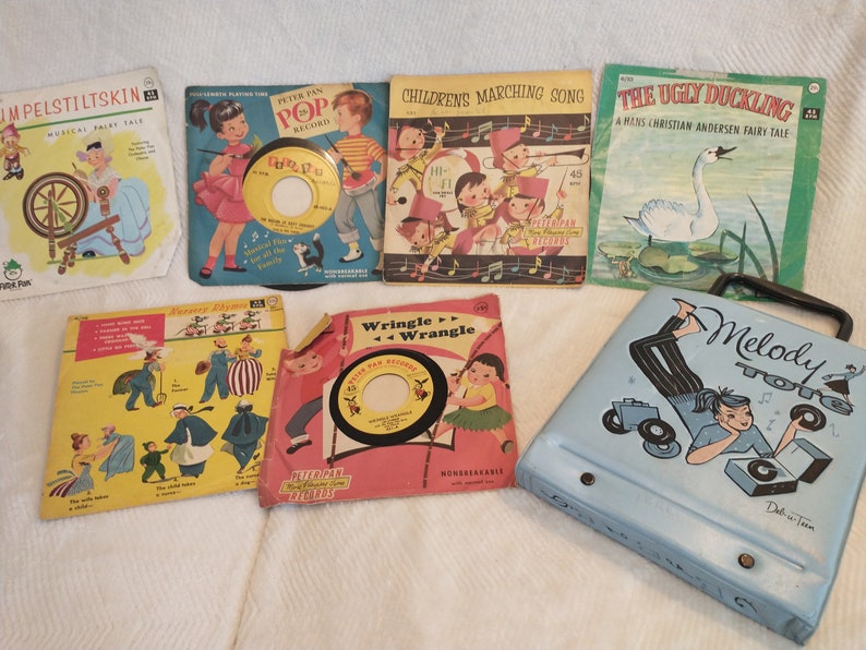 May include: A collection of vintage children's record players and records. The records feature colourful covers with illustrations of children and animals. The record players are blue and black with a design of a girl listening to music.