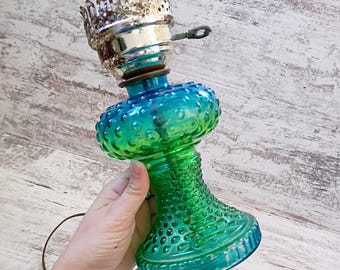 Puede incluir: Una base de lámpara eléctrica de estilo vintage con un cuerpo de vidrio con patrón de puntos que transiciona de un verde vibrante en la base a un turquesa brillante en la parte superior. Incluye un cuello metálico plateado con borde festoneado.