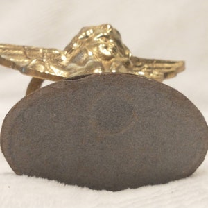 May include: A gold-colored angel figurine with wings outstretched, sitting on a round, gray base.
