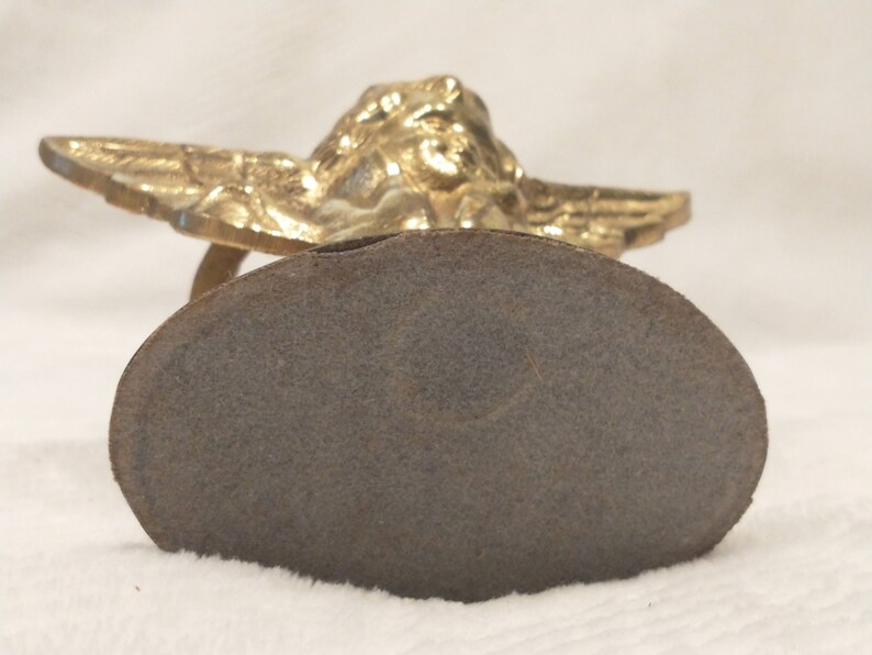 May include: A gold-colored angel figurine with wings outstretched, sitting on a round, gray base.