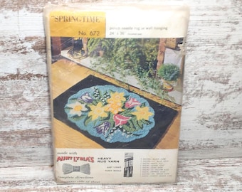 May include: Vintage "Springtime" punch needle rug kit featuring a floral design with yellow, pink, and blue flowers on a blue background. The kit includes heavy rug yarn and a punch needle. The kit is made by Aunt Lydia's and is number 672.