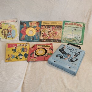 May include: A collection of vintage children's record albums and a record player case. The albums feature colourful illustrations and titles such as "Rumpelstiltskin", "Peter Pan", "Children's Marching Songs", and "The Ugly Duckling". The record player case is blue with a cartoon of a boy playing records.