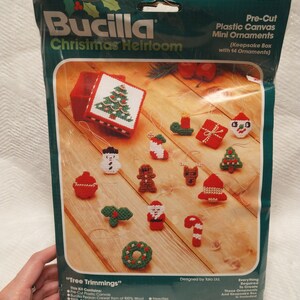 May include: A Bucilla Christmas Heirloom craft kit with 14 pre-cut plastic canvas mini ornaments. The kit includes everything needed to create the ornaments, including yarn, needles, and a keepsake box. The ornaments feature a variety of Christmas themes, such as a snowman, a gingerbread man, and a Santa Claus.