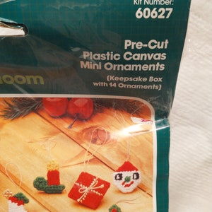 May include: A plastic canvas craft kit with 14 pre-cut mini ornaments for Christmas. The ornaments include a snowman, a Christmas tree, a stocking, a gift, a candle, and a reindeer. The kit comes with a keepsake box. Kit number 60627.