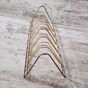 May include: A vintage gold-toned metal record holder. The holder has a triangular shape with multiple curved dividers to hold vinyl records. The design is simple and elegant, suitable for a retro or mid-century modern aesthetic.