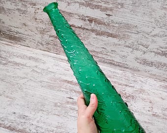May include: A tall, slender, emerald green glass bottle featuring a textured surface with a repeating wave-like pattern. The bottle has a narrow neck that tapers towards a small, circular opening at the top, crafted from translucent green glass.