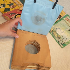 May include: A blue vinyl record carrying case with a black handle. The case is open and has a stack of brown paper record sleeves inside. The text "Return to Sender" is written on the sleeves.