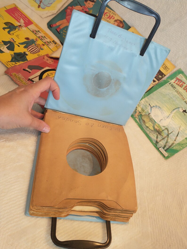 May include: A blue vinyl record carrying case with a black handle. The case is open and has a stack of brown paper record sleeves inside. The text "Return to Sender" is written on the sleeves.
