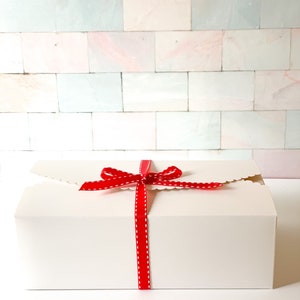 May include: A white gift box with a red ribbon tied in a bow. The ribbon has white polka dots.