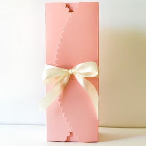 May include: A pink gift box with a scalloped edge and a white satin ribbon tied in a bow.