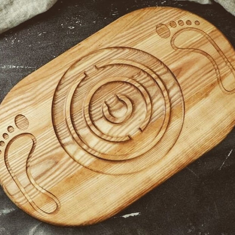 May include: A wooden serving tray with a circular maze design in the center. The tray has two carved footprints on either side of the maze.