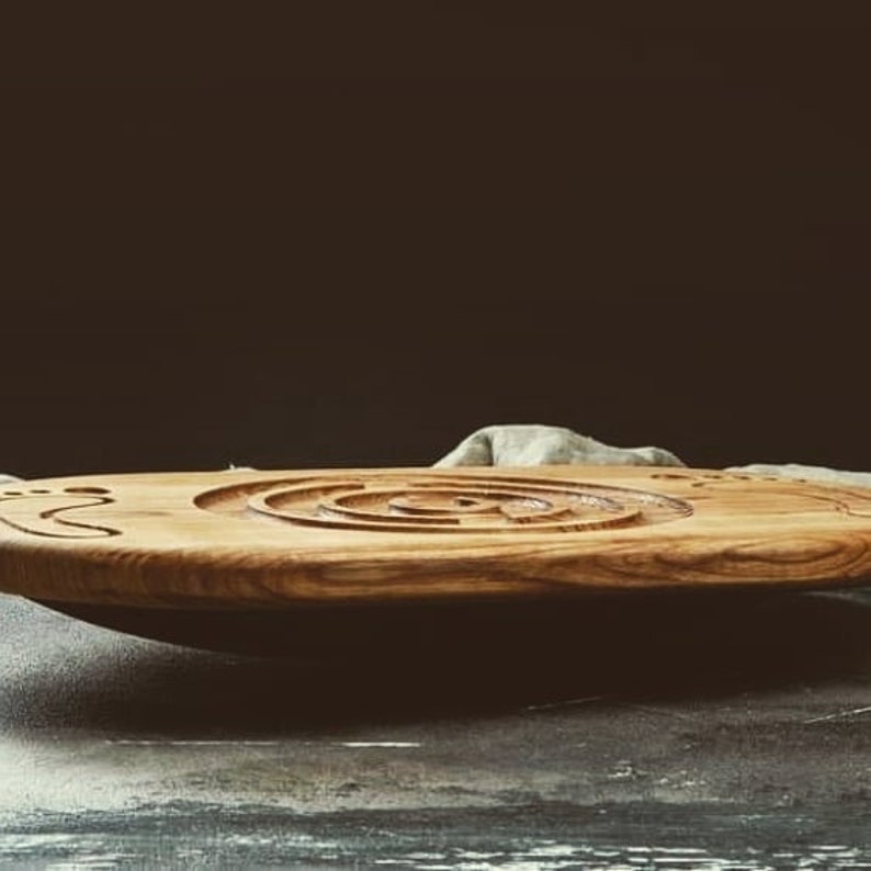May include: A wooden serving tray with a carved maze design. The tray is brown and has a natural wood finish. It is sitting on a gray surface.