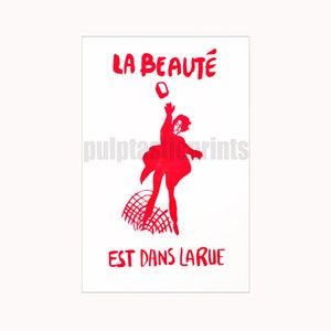 May include: Red and white poster with the text "LA BEAUTÉ EST DANS LA RUE" and a silhouette of a person throwing a brick in the air.