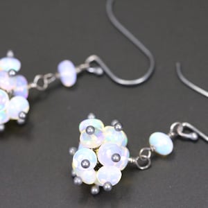 May include: A pair of silver earrings featuring a cluster of iridescent white opal beads. The beads are arranged in a spherical shape and are accented with small silver beads.
