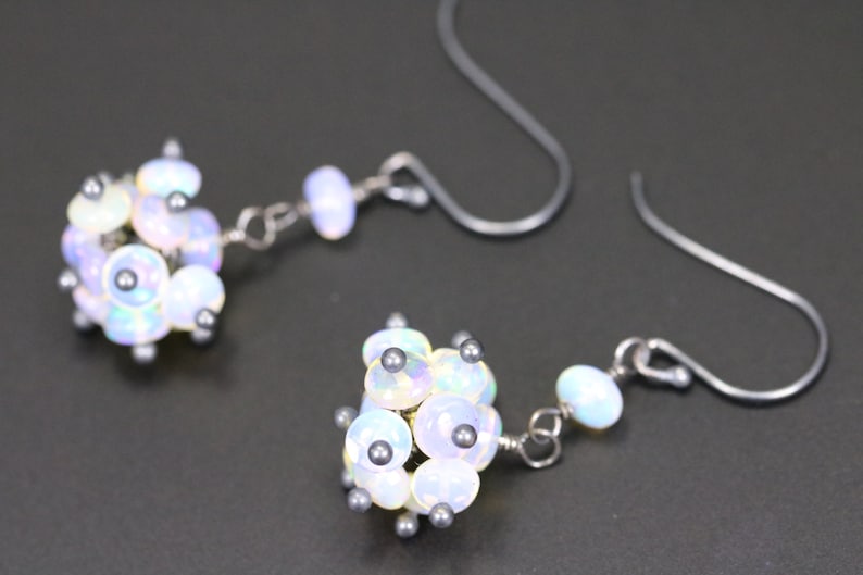 May include: A pair of silver earrings featuring a cluster of iridescent white opal beads. The beads are arranged in a spherical shape and are accented with small silver beads.