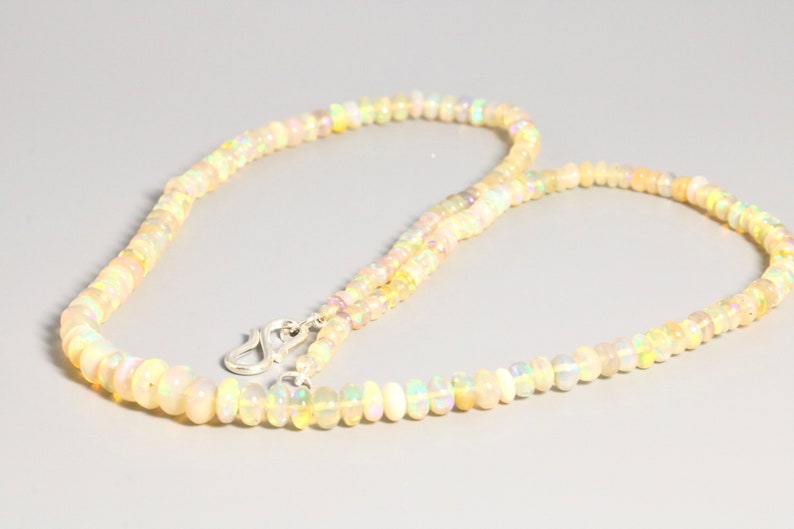 May include: A delicate necklace made of small, iridescent opal beads. The necklace is strung on a silver chain and has a silver clasp.