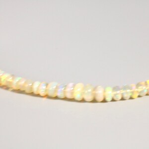May include: A delicate necklace made of small, white opal beads. The beads are iridescent and reflect light in a rainbow of colors.