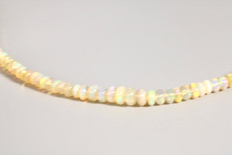 May include: A delicate necklace made of small, white opal beads. The beads are iridescent and reflect light in a rainbow of colors.