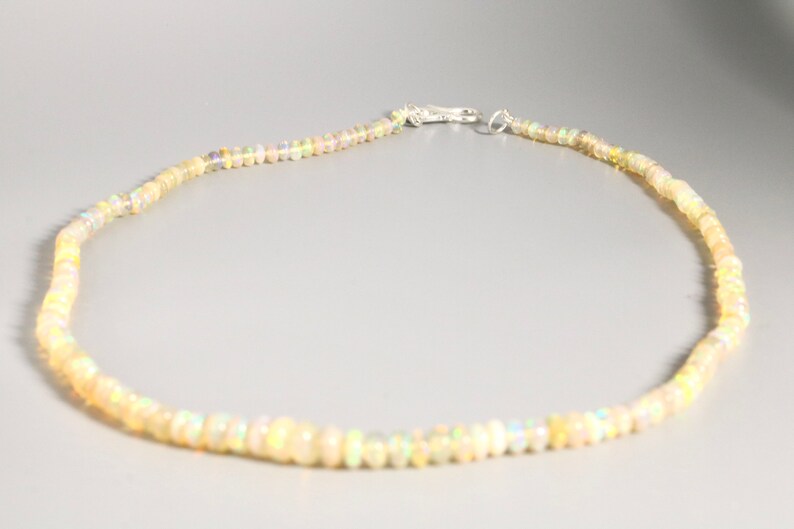 May include: A delicate necklace made of small, iridescent white opal beads. The necklace is strung on a silver chain and has a silver clasp.