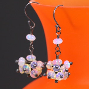 May include: A pair of silver earrings with a cluster of iridescent white opal beads and black beads hanging from a silver hook.