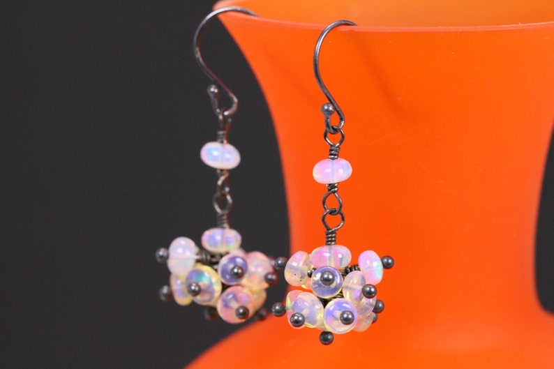 May include: A pair of silver earrings with a cluster of iridescent white opal beads and black beads hanging from a silver hook.