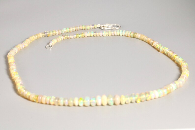 May include: A delicate necklace made of small, iridescent opal beads. The necklace is strung on a silver chain and has a simple clasp.