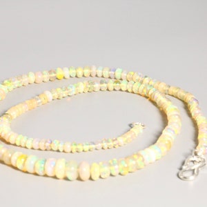 May include: A long necklace made of small, round, iridescent opal beads. The necklace is light yellow in color and has a silver clasp.