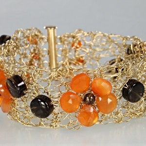 May include: A gold wire bracelet with orange and brown gemstone beads. The bracelet is woven in a delicate pattern and features a clasp closure.