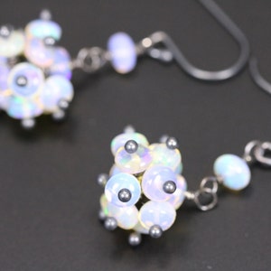 May include: A pair of silver earrings featuring clusters of iridescent white opal stones. Each cluster is composed of several small, round stones.