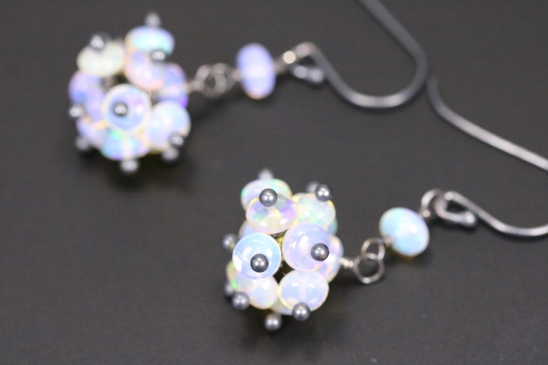 May include: A pair of silver earrings featuring clusters of iridescent white opal stones. Each cluster is composed of several small, round stones.